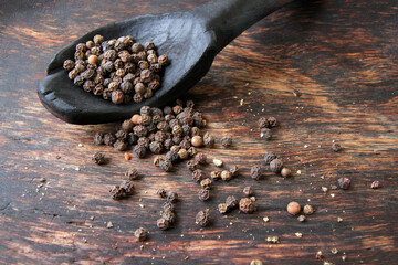 spice black pepper in a black spoon on a wooden background.