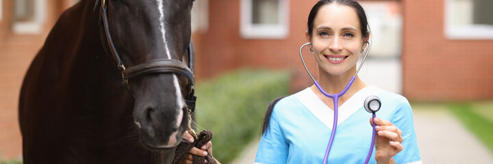 Smiling female veterinarian doctor holding stethoscope next to horse