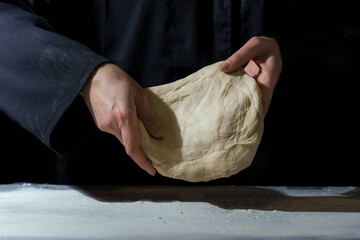 dough in hands on a dark. woman kneads dough on a floured table.