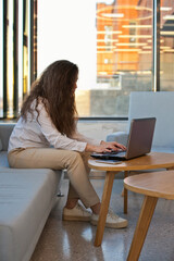 woman sitting on a sofa or couch working on a laptop in the office with big windows