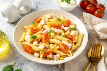 Pasta salad with ham, mozzarella, corn, tomatoes and olive oil in a ceramic plate on a light culinary background. Traditional Italian dish penne rigate with cheese and vegetables	