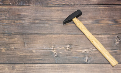 A construction hammer with a wooden handle lies on the brown floor on the right. A hammer on wooden boards.
