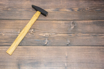 A construction hammer with a wooden handle lies on the brown floor on the left. A hammer on wooden boards.
