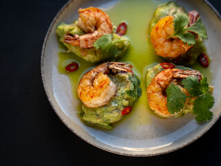Appetizer with shrimps served with guacamole and greens on white plate on black background. Delicious, beautiful, healthy snack. Modern cuisine