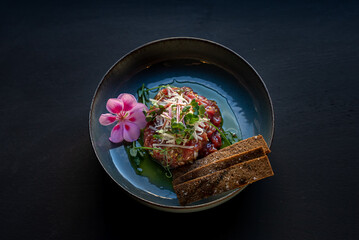 Appetizer beef tartare served with flower and toast on black background. Delicious, beautiful, healthy snack. Modern cuisine. 