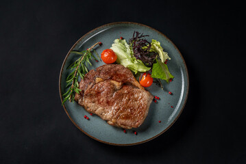 Juicy steak medium rare beef with spices, greens and vegetables on plate on black background. Tasty dinner with friends in restaurant. Copy space