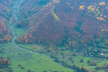 Small village at the foot of the greatest Caucasus mountains on an autumn day. Beautiful landscape of autumn mountains