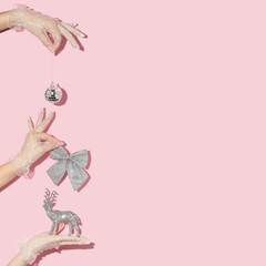 Christmas and New Year creative pattern with hands in lace gloves holding christmas decoration on pastel pink background. 80s or 90s retro fashion aesthetic celebration concept.