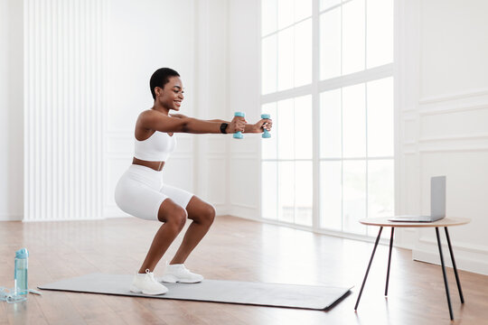 Young black woman exercising with dumbbells in front of laptop