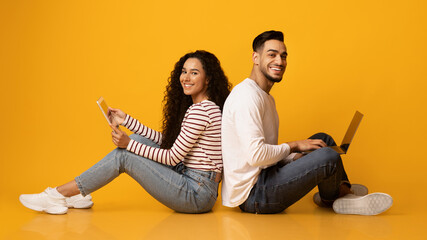 Cheerful arab couple sitting back to back with laptop and digital tablet