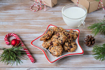 Oatmeal cookies with chocolate and cranberries on a star-shaped plate and milk in a glass transparent cup for Santa Claus on a wooden background.