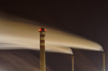 Dymiące kominy fabryki nocą.