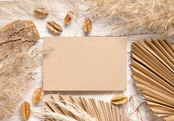 Blank card on white wooden table near dried plants, palm leaves and pampas grass