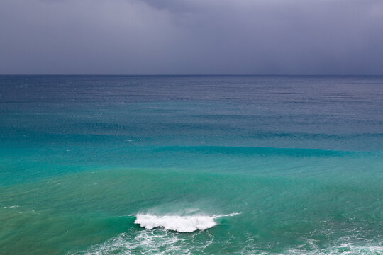 Impressive background photo of the Mediterranean. The green, turquoise, blue, navy blue colors of the sea combine with the gray color of the rain clouds. Small waves accompany this beautiful view.