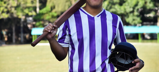 Male cricket coach holds helmet and bat in the green grass court of school before teaching cricket sport to students at school in the afternoon of the day.