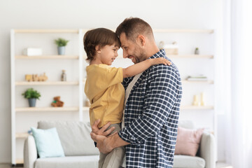 Fototapeta premium Father and son connection. Happy daddy holding his little boy on hands, both bonding foreheads and smiling to each other