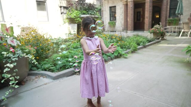 Asian little girl popping bubbles in the courtyard during a sunny day