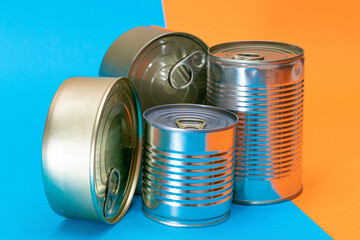 A Group of Stacked Tin Cans with Blank Edges on Split Blue and Orange Background. Canned Food. Different Aluminum Cans for Safe and Long Term Storage of Food. Steel Sealed Food Storage Containers