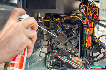 Maintenance and cleaning of the insides of the computer. Man's hand holds a cylinder of compressed air and cleans the insides of the computer - obrazy, fototapety, plakaty