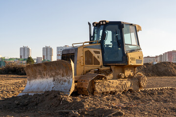 Photo of a yellow muddy excavator digging the ground at a construction site at the background of city. Constructional concept