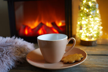 Cup with blanket over fireplace on wooden table. Winter and Christmas holiday concept