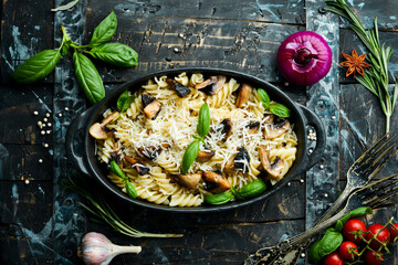 Pasta with mushrooms, parmesan cheese and basil in a black pan. Top view.