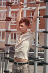 Portrait of a young guy doing sports on the horizontal bar. Outdoor playground for athletes.