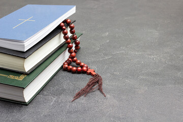 Books and rosary on black. Cross on cover of top book.