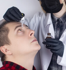 Close-up of eye drops. A man at the doctor appointment, who drips drops into the patient eyes. Concept treatment conjunctivitis, eye fatigue, glaucoma. Viral or bacterial infections