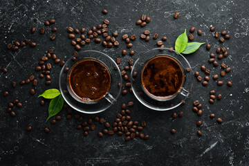 Two cups of fragrant coffee and coffee beans on a black stone background. Top view. Free space for...