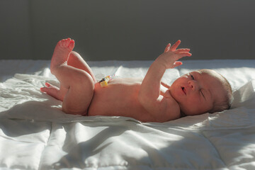 bebe recién nacido con la pinza del cordón umbilical juega mientras toma el sol de la mañana