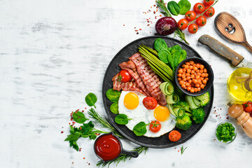 English breakfast: chickpeas, avocados, scrambled eggs, bacon vegetables on a black stone plate. Top view. Free space for text.