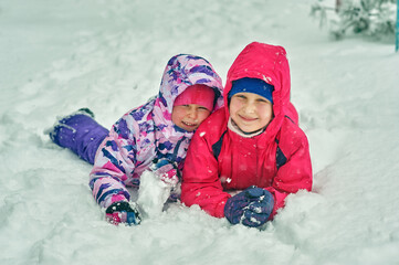 Funny children are lying in the snow . Two girlfriend girls enjoy the fresh snow on a walk in the park