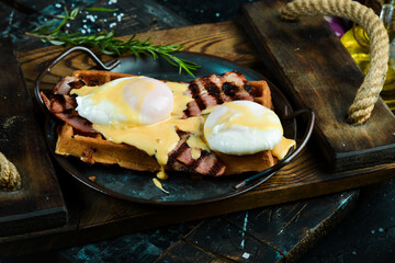 Sandwich with poached egg and bacon on a plate in the hands of a chef On a black background. Belgian waffles.