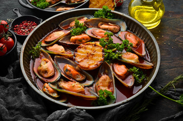Metal tray with mussels cooked in tomato sauce with garlic, parsley and lemon. On a black stone background.