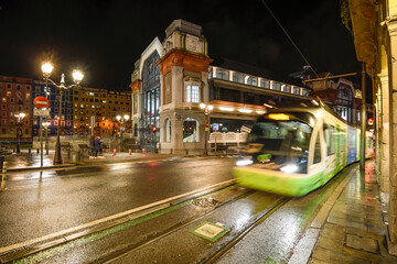 Fototapeta na wymiar Bilbao tram circulating next to the Ribera market at night and raining