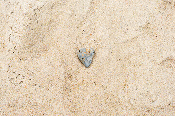 Heart-shaped gray sea rock on sandy beach