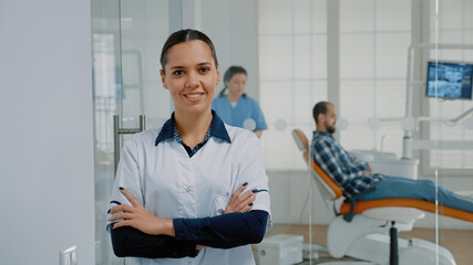 Obraz premium Portrait of woman with stomatologist occupation standing in oral care cabinet and smiling. Caucasian dentist with professional expertise looking at camera prepared for patient consultation