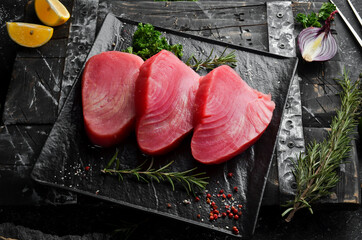 Fresh juicy tuna steak on a black stone plate. On a dark background. Top view.