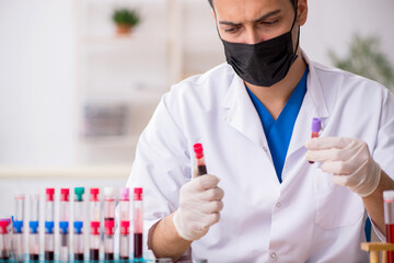 Young male biochemist testing blood samples in pandemic concept