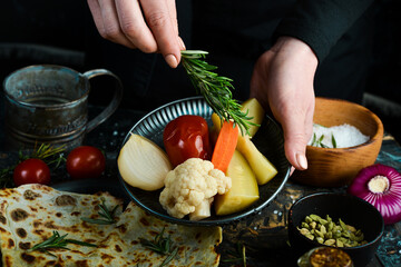 Pickled cucumbers, tomatoes, onions and cabbage on a plate in the hands of a chef on a black background.