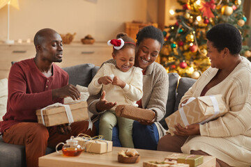 Warm-toned portrait of happy African-American family opening Christmas gifts while enjoying holiday...