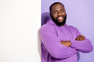 Portrait of attractive cheerful guy demonstrating copy space health care information folded arms isolated on violet purple color background
