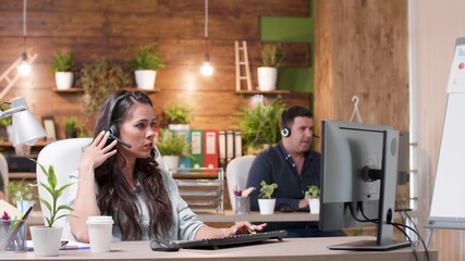 Support customer woman wearing headphones talking into microphone with call center customers using helpline. Caucasian female consultant providing telemarketing service in startup business office