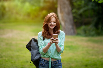 Cheerful redhead student girl using smartphone outdoors, texting with friends