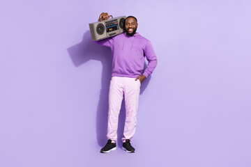 Full length body size view of attractive cheerful guy wearing hoodie carrying boombox isolated over...