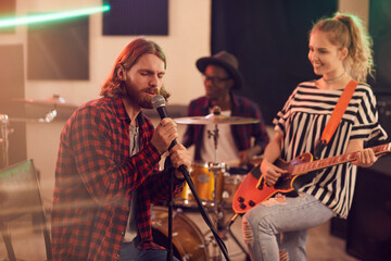 Portrait of bearded man singing to microphone during rehearsal or concert with music band in studio, copy space