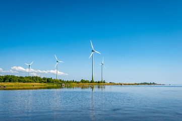 Wind mill generating electricity at the seaside. Wind-turbine on outdoor with sun and blue sky,...
