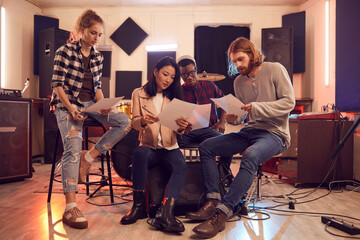 Full length portrait of multi-ethnic band writing music together, all holding lyric sheets while...