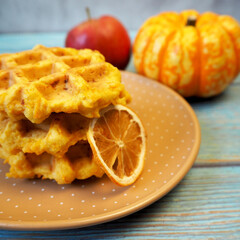 Belgian gluten-free pumpkin waffles lie on a brown plate with a dry slice of lemon, pumpkin, apple on a blue wooden table. breakfast
